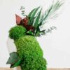 White concrete vase upright with preserved green reindeer moss, ball moss, and eucalyptus branches on wooden surface.