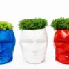 Geometric concrete head planters in blue, white, and red, filled with green moss on a plain white background.