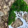 Side angle of round tree of life moss art with white cutout frame and pinecones against natural tree bark.