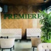 Green moss letters spelling PREMIERE on a wooden chevron wall above tufted booth seating in a lounge.