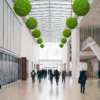 Bright green reindeer moss balls suspended from the ceiling in a large museum atrium.
