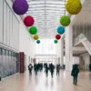 Multicolored reindeer moss balls hanging from a high glass ceiling in a spacious modern hall.