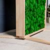 Close-up of the natural wood frame and stabilizing base feet on a green ball moss room divider panel