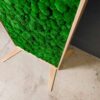 Green ball moss room divider panel with natural wood frame and freestanding base feet on concrete floor