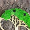Wooden tree wall art decorated with bright green preserved moss and small pine cones on a tree bark background.