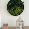 Round green moss wall art above a wooden table holding a ceramic house figurine and a white candle lantern.