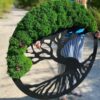 Round black wooden Tree of Life wall art with green reindeer moss foliage and small pine cones held outdoors