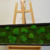 Panoramic moss wall art with mixed ball and flat green moss in a black frame displayed on a wooden easel.