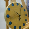Round light wood wall clock with blue circular epoxy resin hour markers and black hands on an easel stand