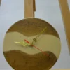 Round wood wall clock (9") with milky white epoxy resin river, ornate gold hands, and red second hand on an easel