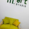 Green moss letters spelling m.art mounted on a white wall above a yellow-green sofa