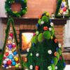 Pyramidal green moss Christmas tree with mini baubles displayed near a fireplace with a matching moss wreath.