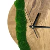 Close-up of round oak wall clock showing natural wood grain, bright green moss strip, and black clock hands