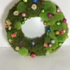 Round Christmas wreath of textured green moss adorned with colorful mini baubles, pine cones, and holiday ornaments.