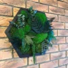 Hexagon moss wall art with preserved ferns and ball moss in a black frame on an exposed brick wall.