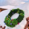 Green moss holiday wreath with colorful bauble ornaments displayed on a snow-covered wooden surface