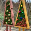 Decorative wooden moss Christmas trees with ornaments and stars displayed on an outdoor wooden table.