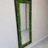 Rectangular wall mirror in a black frame with green ball moss inner border mounted on a white wall