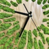 Wooden wall clock detail with black hands and organic cutouts filled with green preserved reindeer moss.