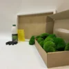 DIY moss kit with green ball moss in a cardboard box, white frame, glue bottle, spreader, and gloves on a white surface