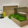 DIY moss wall art kit with green reindeer moss in a box, white frame, adhesive bottle, spreader, and gloves