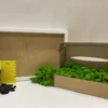 DIY kit with white frame, glue bottle, black gloves, scraper, and cardboard box filled with green reindeer moss