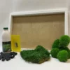 White frame with green flat moss, ball moss clusters, glue bottle, yellow scraper tool, and black gloves.