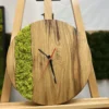 Round wooden wall clock with green moss inlay and black and red hands, displayed on a wooden easel