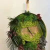 Round moss wall clock with preserved green foliage and natural wood slice center, displayed on a wooden easel.