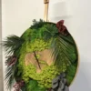 Side view of round wall clock with preserved green moss, ferns, and central wood cut on a wooden easel.