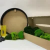 Cardboard box of vibrant green moss beside empty round black frame, glue bottle, spreader tool, and protective gloves