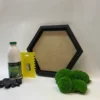 Black hexagon frame with green ball moss, adhesive bottle, yellow spreader, and gloves for DIY moss wall art.