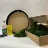 DIY round moss kit with black frame, glue bottle, scraper, gloves, and open cardboard box filled with green moss.