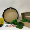 DIY moss wall art kit with round black wooden frame, green preserved moss, dried flowers, glue, scraper, and cardboard box
