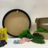 Round moss art kit components including black wooden frame, green moss, dried flowers, glue bottle, and applicator.