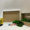 DIY moss kit materials with a white rectangular frame, craft glue, tools, preserved moss, and small dried flowers.