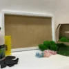 White frame DIY moss craft kit with adhesive bottle, yellow spreader, gloves, assorted dried flowers, and green moss.