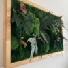 Preserved moss wall art with fern leaves and wood accents in a natural wooden frame, viewed from an angle.