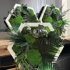 Three white hexagonal moss wall art frames with ball moss, ferns, and preserved foliage on a wooden table.