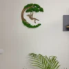 Wooden girl on a swing moss wall art hanging on a white wall above potted palm leaves.