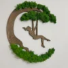 Wooden silhouette of a girl on a swing decorated with vibrant green moss on a white wall.
