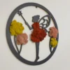 Angled view of circular fairy wall art with black frame and colorful moss accents hanging on a white wall