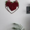 Red moss heart wall decor mounted on a white wall above indoor palm leaves.