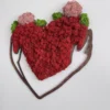 Red, pink, and green moss wall art inside a dark wood outline of arms forming a heart, mounted on a white wall.