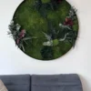 Round preserved moss wall art with greenery mounted on a white wall above a gray couch