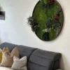 Angled view of round preserved moss and plant wall art mounted above a gray sofa