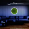 Backlit round green moss wall art displayed on a paneled wall in a modern living room above a sectional sofa