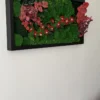 Rectangular preserved green moss wall art with red flowers and eucalyptus leaves in a black wooden frame on a white wall