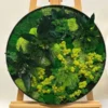 Round preserved moss wall art with mixed green foliage in a black frame displayed on a wooden easel
