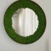 Round wall mirror framed with green reindeer moss in a slim circular frame on a white wall